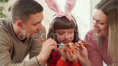 爸爸妈妈帮女儿用画笔装饰复活节彩蛋.. 幸福的家庭一起准备复活节。
